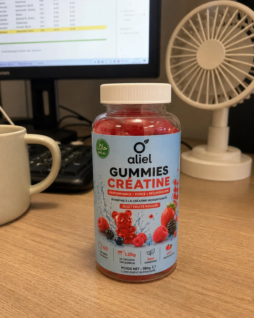 Smartphone photo of the aliel GUMMIES CRÉATINE bottle sitting on a wooden desk next to a monitor dis